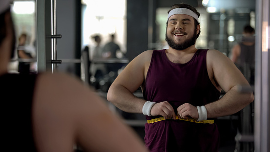 Happy obese man measuring fat waist, satisfied with results of training program